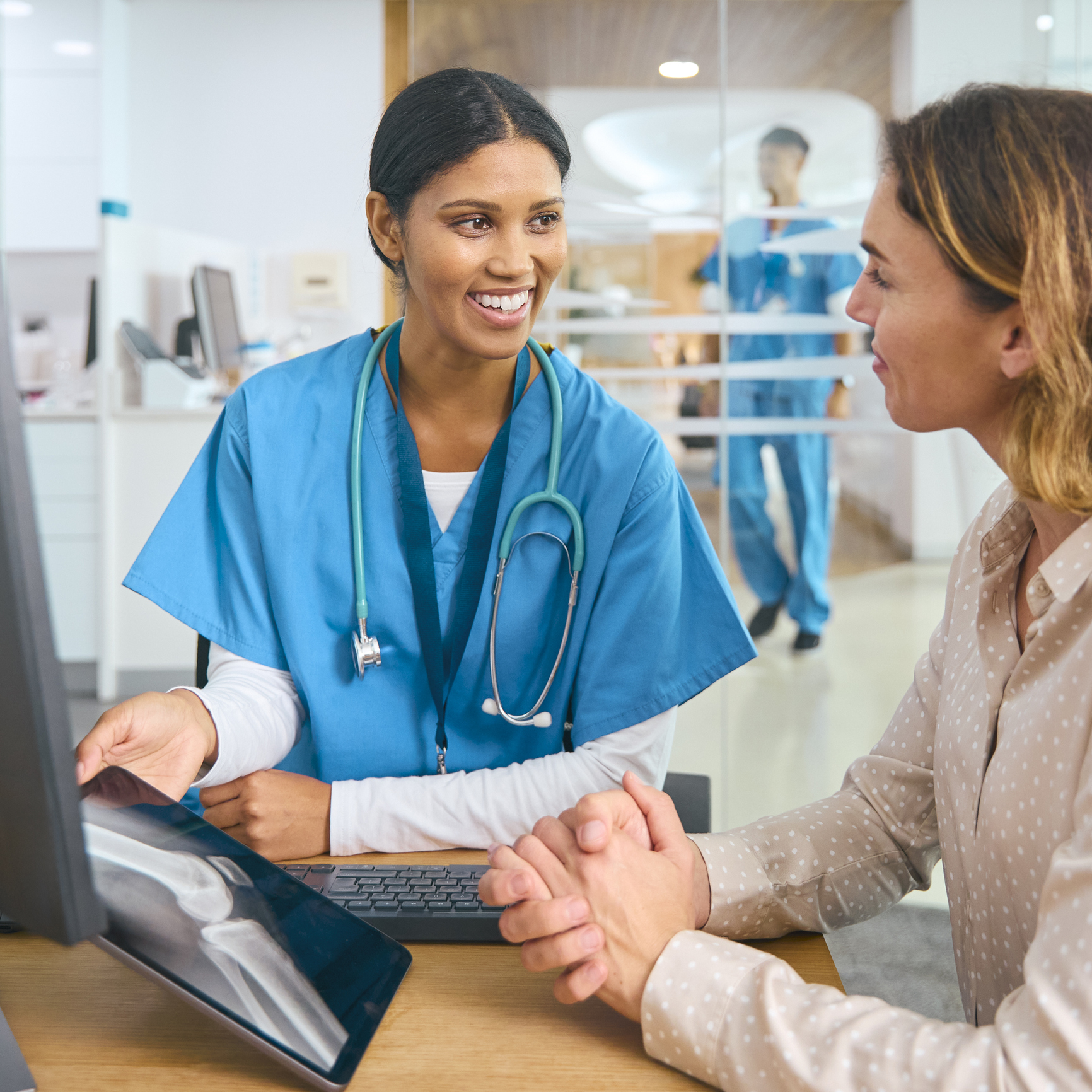 female doctor wearing scrubs at hospital appointment with woman patient looking at digital tablet