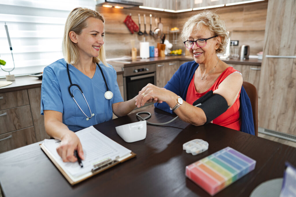 nurse checks the blood pressure of a cheerful elderly woman in a cozy kitchen