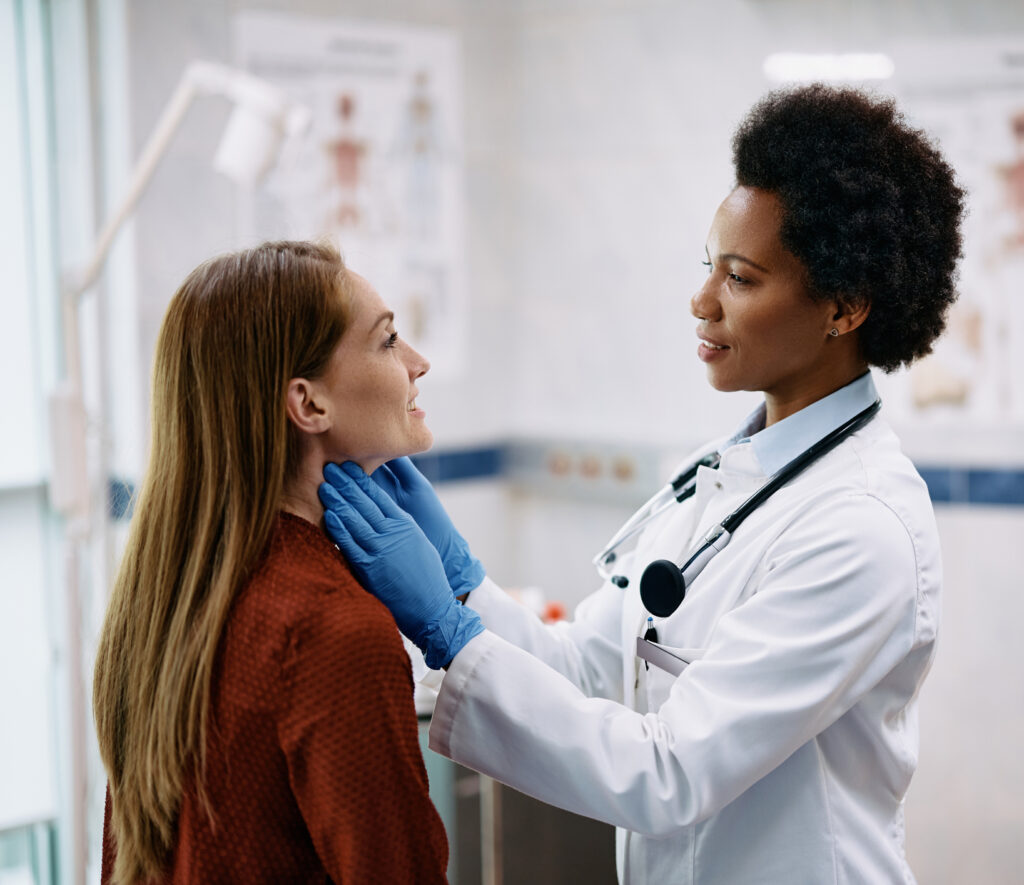 smiling woman having a thyroid exam by black female endocrinologist at medical clinic.